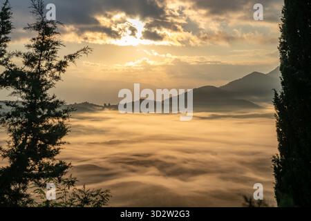 Ein Bergtal am Morgen, wo die Herbstsonne durch die Wolken bricht, um ihr Licht zu werfen, und den Talnebel in Goldfarbe taucht. Stockfoto