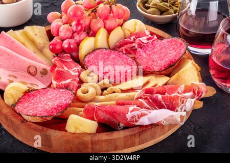 Italienische Antipasti. Wurstplatte mit Käse und anderen Snacks, mit Wein und Oliven, auf schwarzem Hintergrund Stockfoto