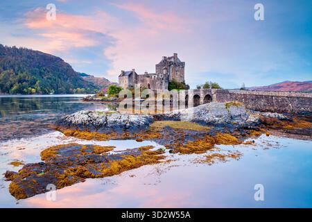 Eilean Donan Castle, Highland, Schottland, an einem hellen Herbstmorgen, wunderschönes rosa-oranges Licht am Himmel und reflektiert im See. Stockfoto