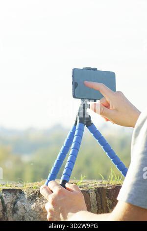 Berühren Sie einen Smartphone-Bildschirm mit dem Finger auf einem Stativ an der Wand. Symbolisiert den Beginn des Films und den Prozess der praktischen Erstellung von Inhalten. Stockfoto