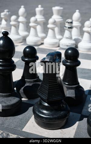 Große schwarz-weiße Schachfiguren auf einem Outdoor-Brett symbolisieren Wettbewerb und Strategie. Stockfoto