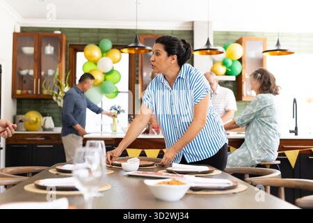 In der Küche, Familie arrangiert Tisch und bereitet sich auf die Feier, plaudert glücklich. Vorbereitung, Party, Kochen, Festlichkeit || Model veröffentlicht Stockfoto
