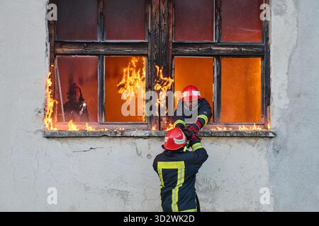 Ein Feuerwehrmann rettet ein Baby aus einem brennenden Gebäude. Der Feuerwehrmann ist in Aktion und rettet das Kind aus der Notsituation. Dieses Bild kann verwendet werden, um Themen von Tapferkeit, Rettungseinsätzen und Rettungsdiensten zu veranschaulichen. || Modell freigegeben Stockfoto
