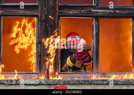 Ein Feuerwehrmann rettet ein Baby aus einem brennenden Gebäude. Der Feuerwehrmann ist in Aktion und rettet das Kind aus der Notsituation. Dieses Bild kann verwendet werden, um Themen von Tapferkeit, Rettungseinsätzen und Rettungsdiensten zu veranschaulichen. || Modell freigegeben Stockfoto