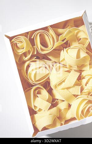 Rohe Pappardelle Nudeln, Nudelnester, in einem Papierkarton, hartes Licht, Blick von oben, keine Leute Stockfoto