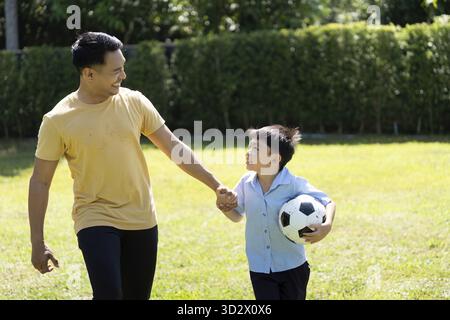 Ein Vater und ein Sohn teilen einen herzerwärmenden Moment, während sie Fußball im Park spielen und betonen, dass Familie und aktives Spiel miteinander verbunden sind Stockfoto