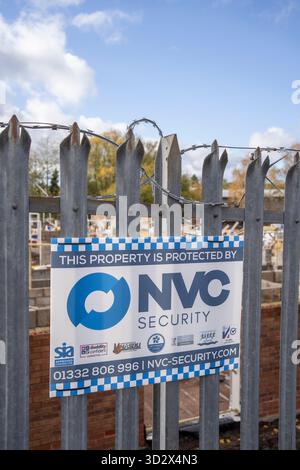 Nahaufnahme eines NVC-Sicherheitsschilds, das eine Baustelle mit Stacheldraht über einem Stahlzaun schützt. Stockfoto