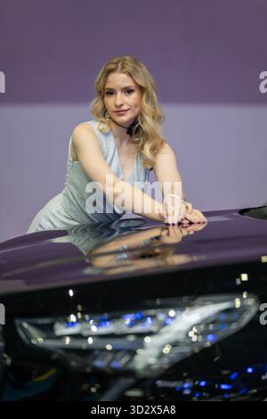 MINSK, WEISSRUSSLAND - 3. JUNI 2025: Eine Frau posiert neben einem neuen Auto auf der Motorshow 2025. Die Motorhaube des Autos reflektiert die Frau und eine helle Stockfoto