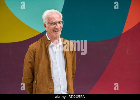 Senior Mann mit Brille posiert und lächelt, zeigt einen glücklichen und gesunden Lebensstil vor einem lebendigen, abstrakten Hintergrund Stockfoto
