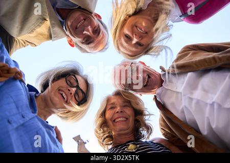 Glückliche, ethnische Seniorenfreunde in einem fröhlichen Outdoor-Kreis, die nach unten schauen, lachen und gemeinsame Zeit und Gesellschaft genießen Stockfoto