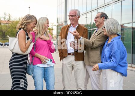 Eine Gruppe glücklicher Seniorenfreunde teilt gern etwas auf einem Mobiltelefon, lächelt und lacht gemeinsam im Freien Stockfoto