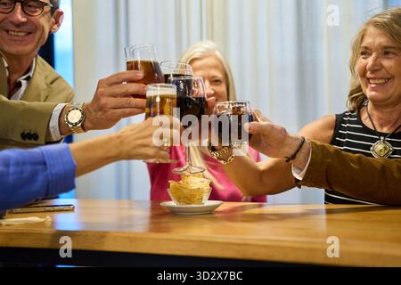 Glückliche Seniorenfreunde, die mit Wein- und Biergläsern anstoßen, Freundschaft feiern und gute gemeinsame Zeiten feiern Stockfoto