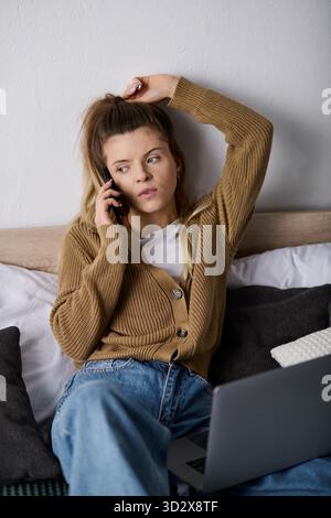 Eine junge Frau entspannt sich in ihrer gemütlichen Wohnung, telefoniert am Telefon und genießt ihren Tag im Bett. Stockfoto