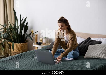 Eine junge Frau entspannt sich im Bett, benutzt ihren Laptop in einer schicken Wohnung und genießt einen faulen Tag. Stockfoto