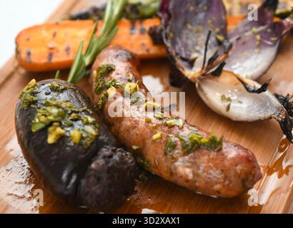 Gegrillte Würstchen mit gegrilltem Gemüse auf hölzernem Schneidebrett. Stockfoto