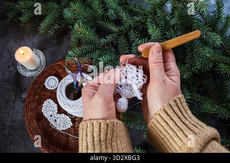 Nahaufnahme eines handgemachten weißen Weihnachtsengels, der mit einer Häkelnadel gemacht wird. Weihnachtsbasteln und DIY-Dekorationskonzept. Stockfoto