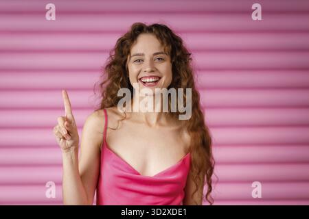 Glückliche, lächelnde junge Frau, die einen Finger zeigt und in die Kamera blickt Stockfoto