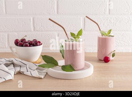 Zwei stilvolle Gläser mit frisch zubereiteten KirschSmoothies und eine Schüssel reifer Kirschen auf der unteren Arbeitsfläche. Ein köstliches, gesundes Getränk. Entgiftung Stockfoto
