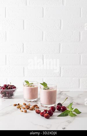 Zwei Gläser frisch zubereiteter Kirsch-Smoothie mit Mandeln und Minze auf einem Marmortisch zwischen Beeren und Nüssen. Ein köstlicher, gesunder Snack. Vertikale Ansicht Stockfoto
