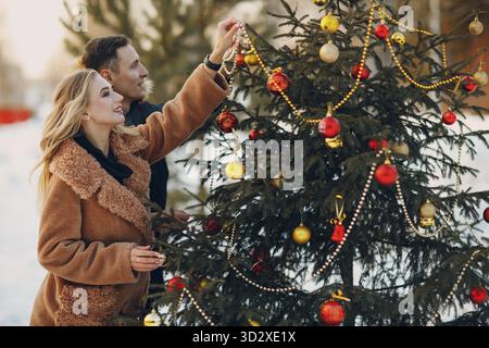 Ein junges erwachsenes Paar schmückt den weihnachtsbaum im Winterwald. Silvester-Feiertagsfeier-Konzept Stockfoto