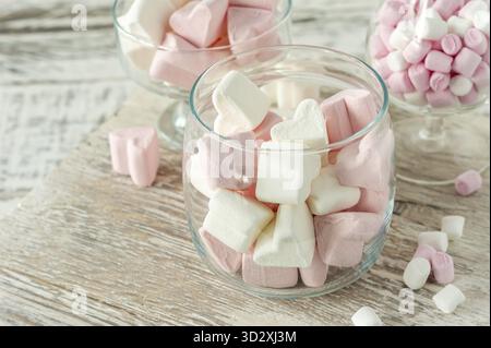 Verschiedene rosafarbene und weiße Marshmallows in Glasbechern auf hölzernem Hintergrund. Marshmallow in Herzform für heiße Schokolade oder Kakao Stockfoto