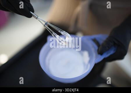 Junge Frau Friseurin, die Haare im Schönheitssalon färbt. Professionelle Haarwurzelfärbung und Mischen von Farbfarben Stockfoto