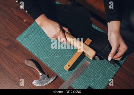 Tanner Frau schneidet Lederwaren in der Werkstatt. Arbeitsprozess des Lederhandwerks Stockfoto