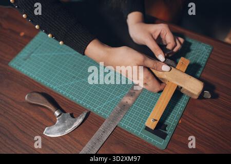 Tanner Frau schneidet Lederwaren in der Werkstatt. Arbeitsprozess des Lederhandwerks Stockfoto