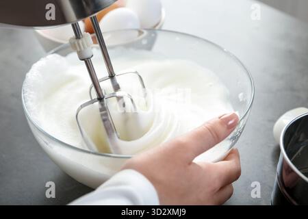 Frau, die Eiweiß mit Mixer am grauen Tisch schlägt, Nahaufnahme Stockfoto