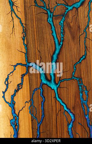 Eine detaillierte Makroaufnahme einer handgefertigten Holzoberfläche, gefüllt mit blauem Epoxidharz, die Flussmuster erzeugt und den Kontrast zwischen diesen hervorhebt Stockfoto