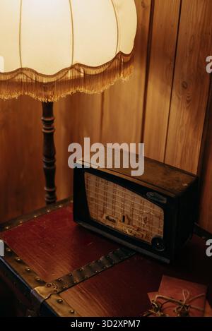 Nahaufnahme eines Vintage-Radios auf einem hölzernen Kofferraum neben einer klassischen Stehlampe mit einem Fransenschirm an einer getäfelten Wand Stockfoto