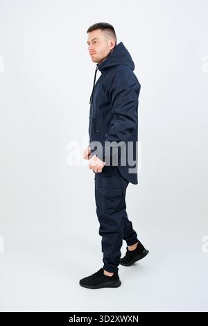 Ein junger Mann steht in entspannter, aber selbstbewusster Pose und trägt ein elegantes, dunkles Outfit, das zeitgenössische Street-Mode widerspiegelt. Die dezente Beleuchtung sorgt für einen zusätzlichen Stockfoto