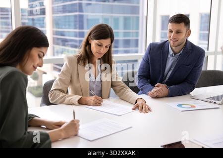 Geschäftspartnerinnen, die beim Treffen einen Vertrag unterzeichnen, sitzen am Tisch Stockfoto