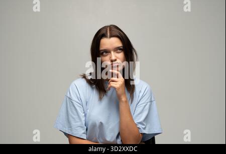 Nachdenkliche Frau, die das Kinn berührt und im Studio-Porträt beiseite schaut Stockfoto