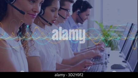 Callcenter-Agenten mit Headsets am Schreibtisch, Tastaturen und Wellengrafik-Overlay Stockfoto