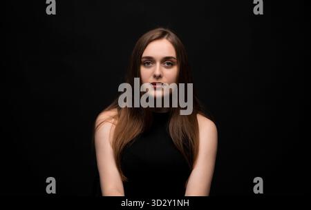 Selbstbewusste junge Frau, die Daumen hoch zeigt und leicht lächelt auf blauem Hintergrund Stockfoto