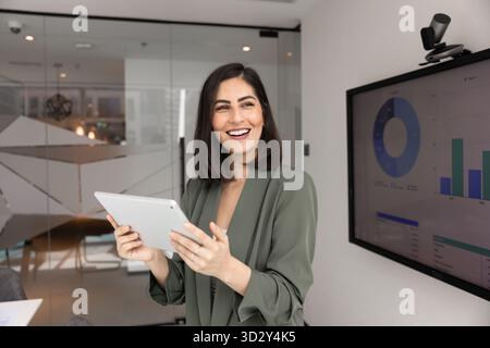 Fröhliche attraktive junge lateinamerikanische Geschäftsfrau, die mit Tablet arbeitet Stockfoto