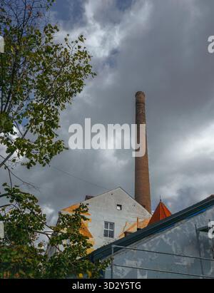 Ein hoher gemauerter Kamin erhebt sich über alten Gebäuden in der Skadarska-Straße in Belgrad, Serbien, unter dramatischen grauen Wolken, die von grünen Blättern eines Baumes eingerahmt werden Stockfoto