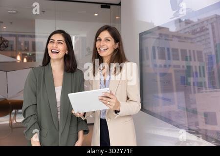 Zwei glückliche Geschäftsfrauen, die sich im Büro für ein Porträt ausgeben Stockfoto
