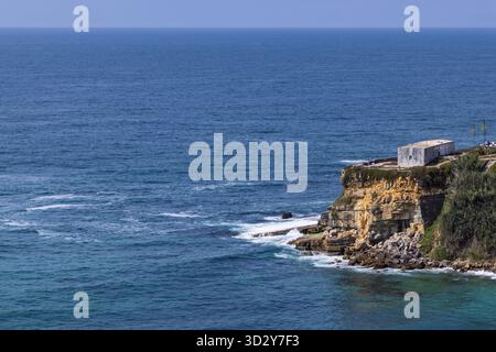 Ein einsames Gebäude befindet sich auf einer zerklüfteten, geschichteten Klippe mit Blick auf die weite, tiefblaue Weite des Atlantischen Ozeans in Magoito, Portugal. Stockfoto