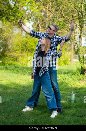 Glücklicher Vater und Tochter nehmen Selfie und zeigen Ein Siegesschild im Park Stockfoto