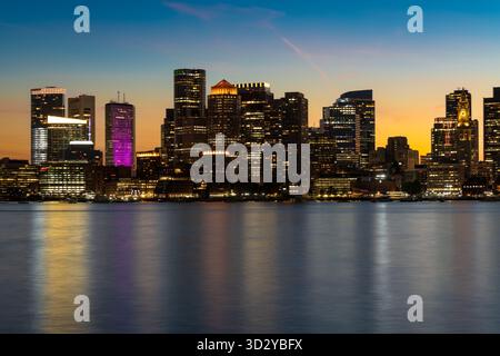 Ein atemberaubender Blick auf die Stadt Boston in der Abenddämmerung mit den beleuchteten Hochhäusern vor einem farbenfrohen Himmel. Stockfoto