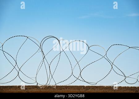 Ein Drahtzaun mit blauem Himmel im Hintergrund. Der Zaun besteht aus Stacheldraht und ist sehr lang Stockfoto