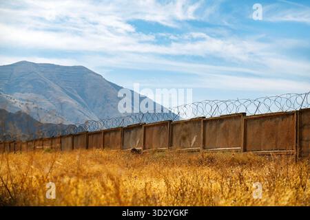 Ein Zaun mit Stacheldraht darauf ist vor einem Berg. Der Zaun ist alt und verrostet Stockfoto