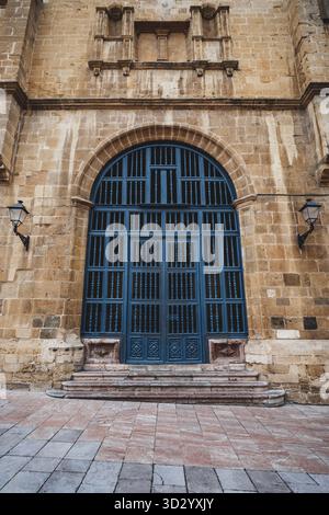 Große bogenförmige blaue Holztür in einer verwitterten Steinfassade eines historischen Oviedo-Gebäudes mit geschnitzten Details, Wandlaternen und abgenutzten Stufen – Dramat Stockfoto