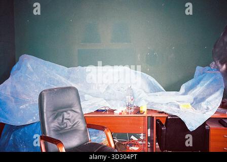 Schreibtisch mit blauem Kunststoff für Renovierungs- und Malzwecke; Markierungen von entfernten Bildern an der Wand sichtbar, in analogen Tönen aufgenommen. Stockfoto