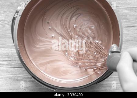 Person, die Goldfarbe in einem Kunststoffbehälter mit einem Metallbesen mischt. Dekorationskonzept Do IT Yourself für Zuhause. Stockfoto