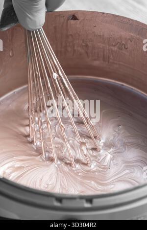 Person, die Goldfarbe in einem Kunststoffbehälter mit einem Metallbesen mischt. Dekorationskonzept Do IT Yourself für Zuhause. Stockfoto