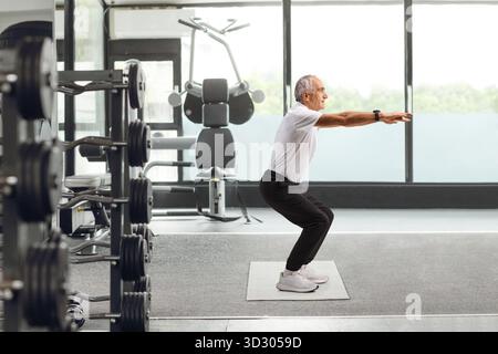 Profilaufnahme eines älteren Mannes, der Squats in einem Fitnessstudio trainiert Stockfoto