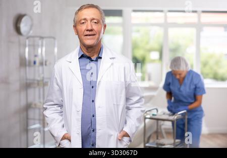Älterer männlicher Arzt posiert in der Arztpraxis Stockfoto